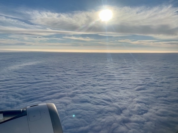 Aerial shot out of the aeroplane, above a blanket of thick, low clouds, with a brilliant sun shining