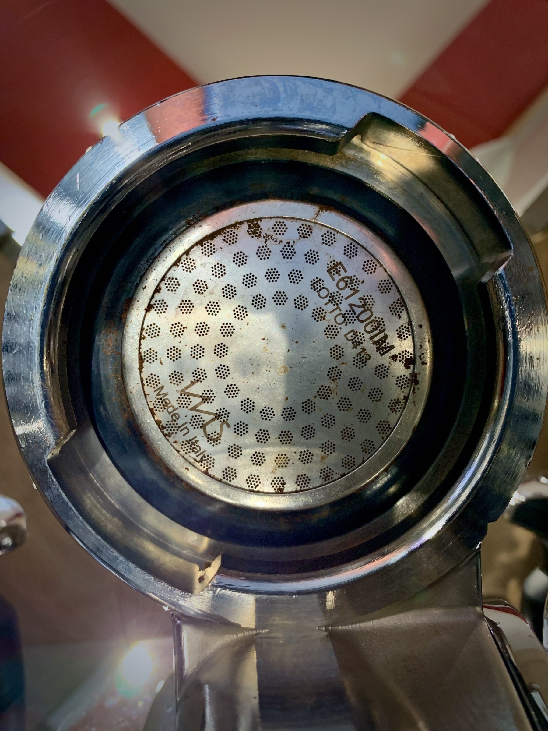 The underside of a E61 style group head, showing coffee grinds stuck to the shower screen and gasket.