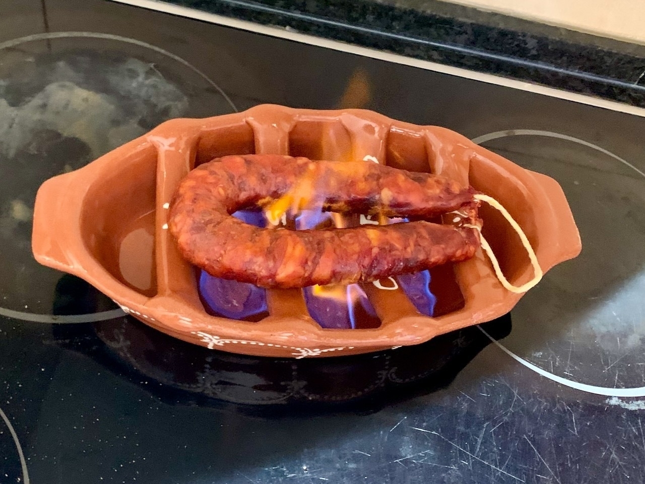 An 'assador', a Portuguese ceramic dish with bars across it, filled with lighter fluid gel that's been set alight, grilling a chouriço Portuguese sausage.