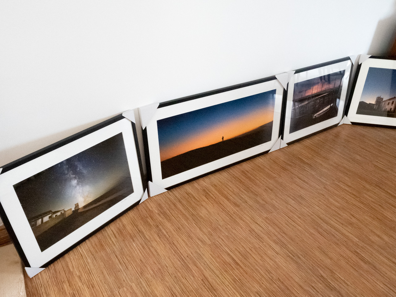 4 printed photographs in picture frames on the floor leaning against a white wall. They are in a black frame with a white mat.